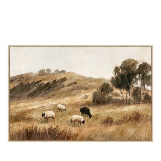 A framed landscape painting depicting sheep grazing in a dry grassy field with rolling hills and trees under a pale sky, shown against a white background.