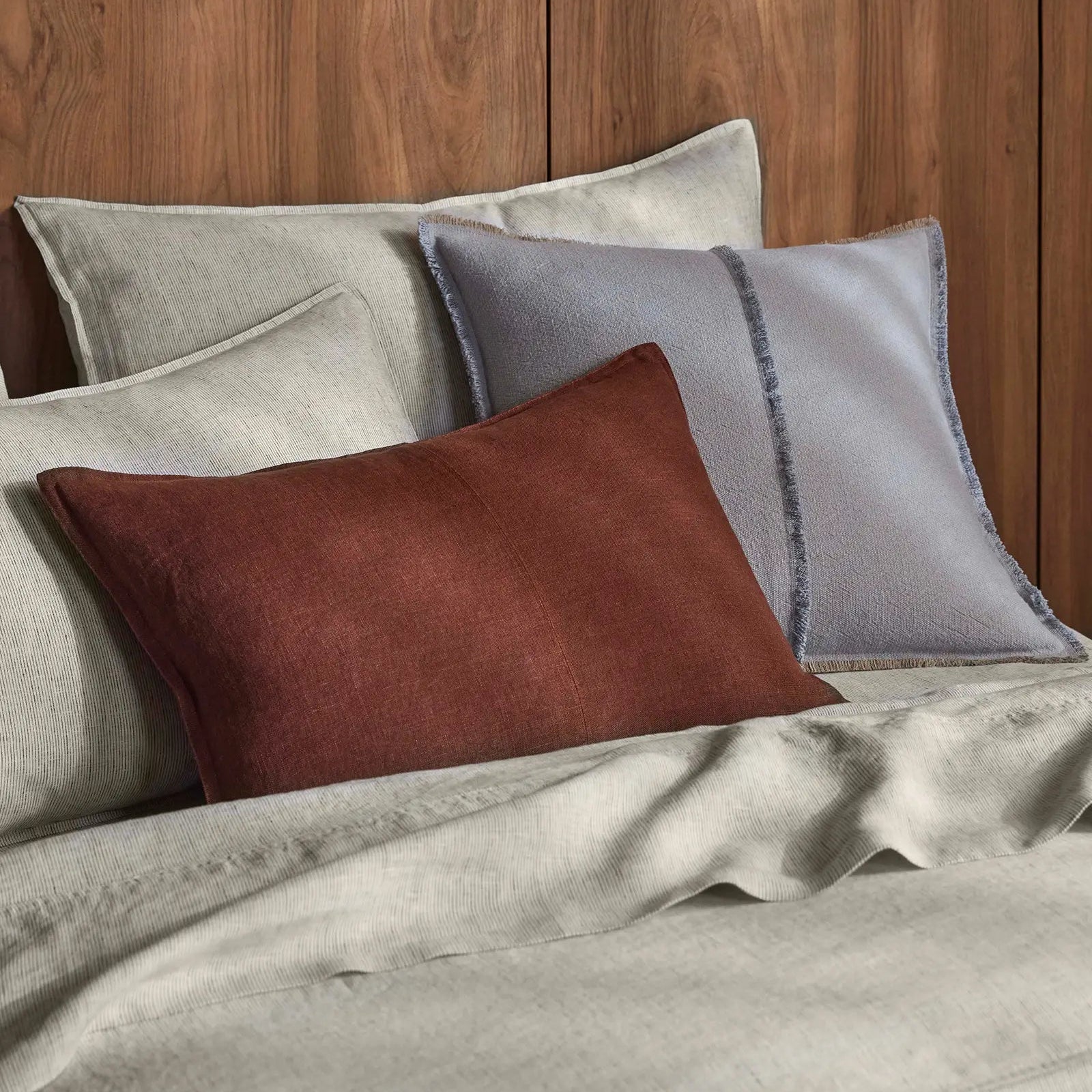 Set of cushions in brown, grey, and beige on a wooden panelled wall.