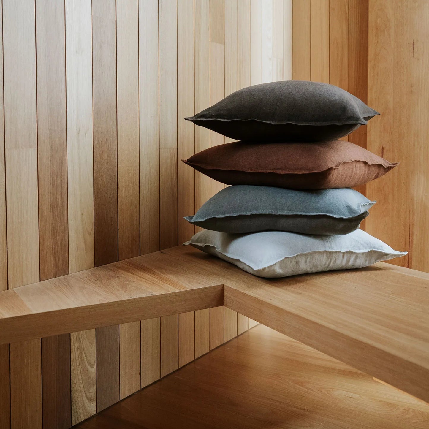 Stack of pillows on a wooden bench against a wooden wall.