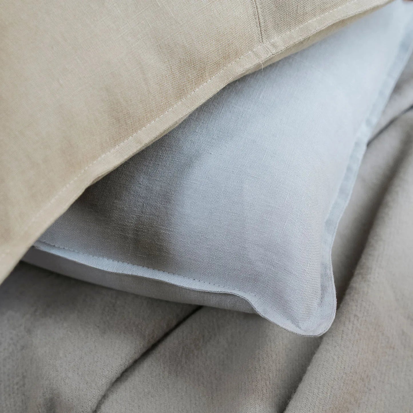 Close-up of a beige pillow with a white pillow inside on a beige surface.