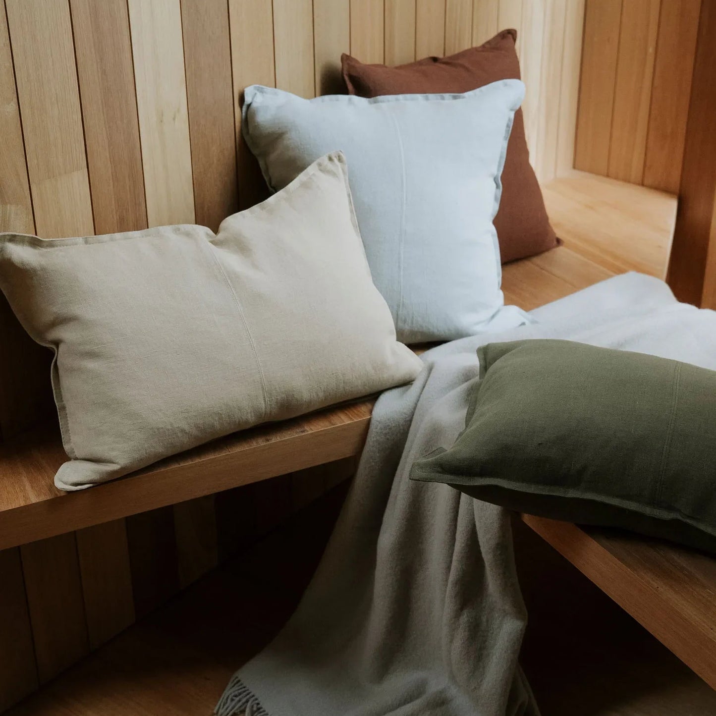 Wooden bench with cushions and a blanket against a wooden paneled wall.