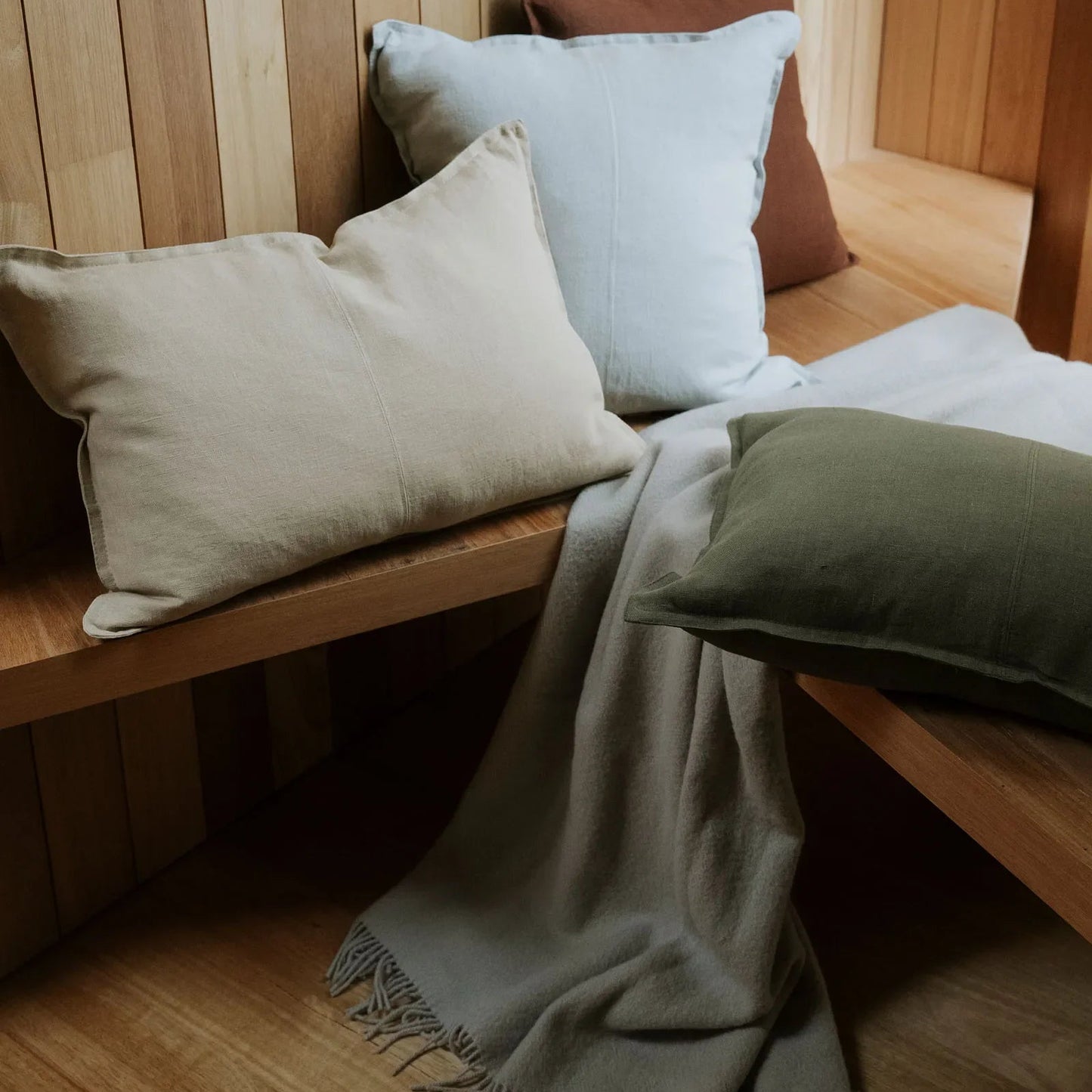 Wooden bench with cushions and a blanket against a wooden paneled wall.