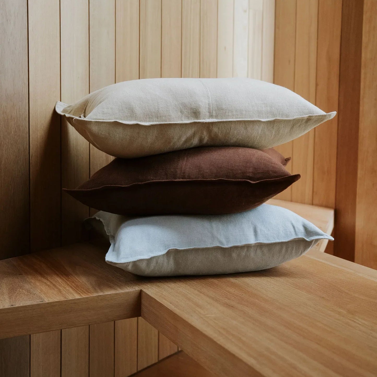 Three pillows stacked on a wooden surface with a wooden wall background