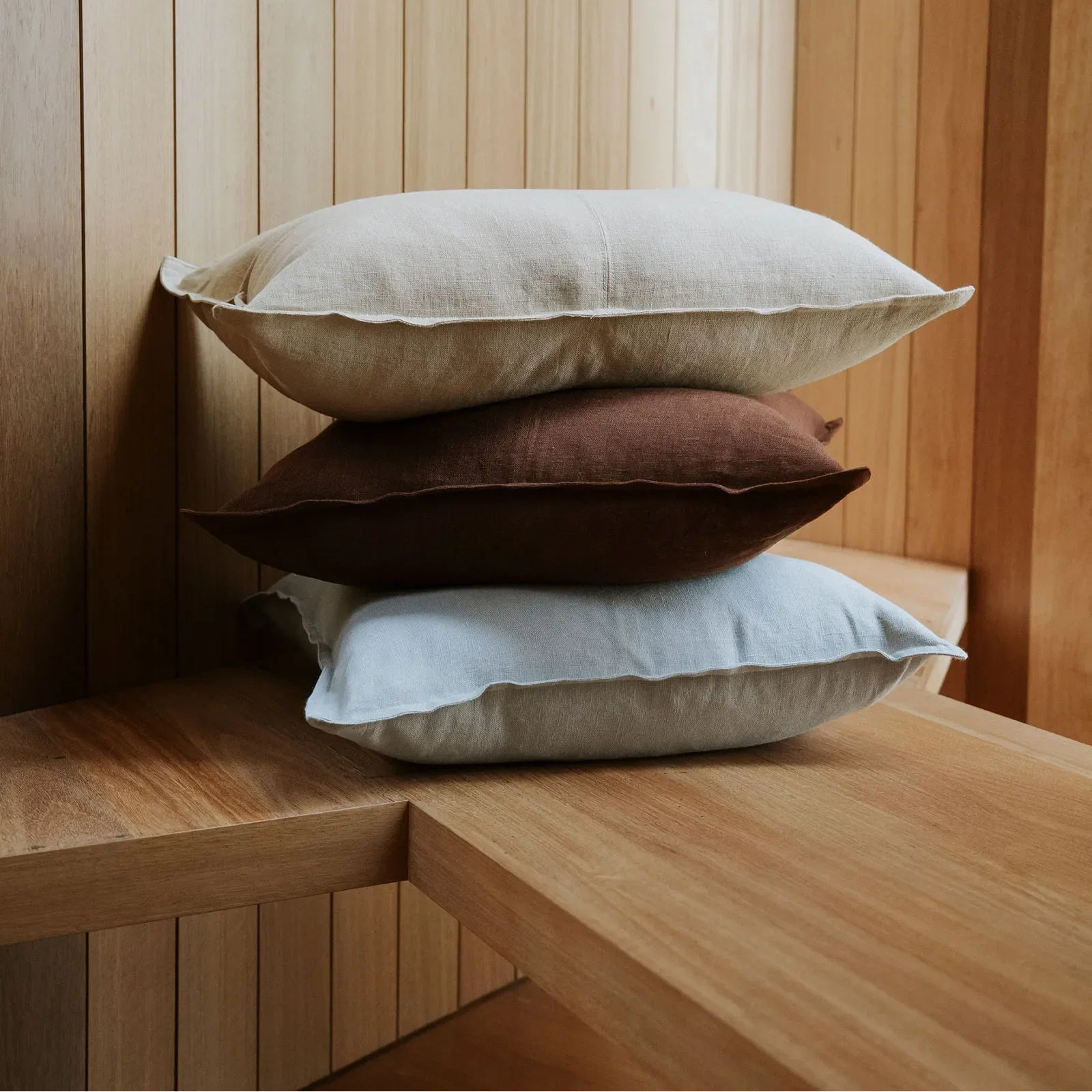 Three pillows stacked on a wooden surface with a wooden panel background