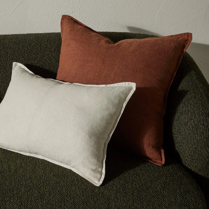 Two pillows, one red and one beige, on a dark green sofa against a neutral wall.