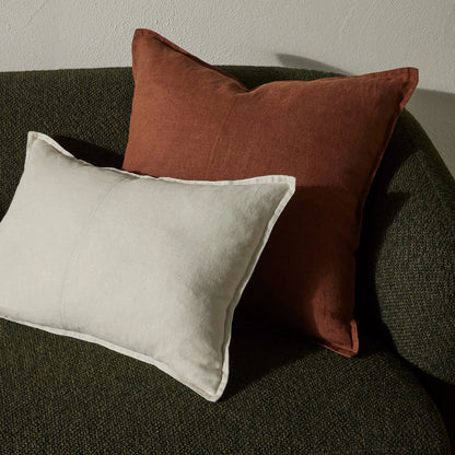 Two cushions, one brown and one beige, on a dark green sofa against a neutral wall.