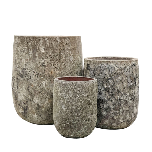 Three stone-textured planters with a green plant on a light gray surface.